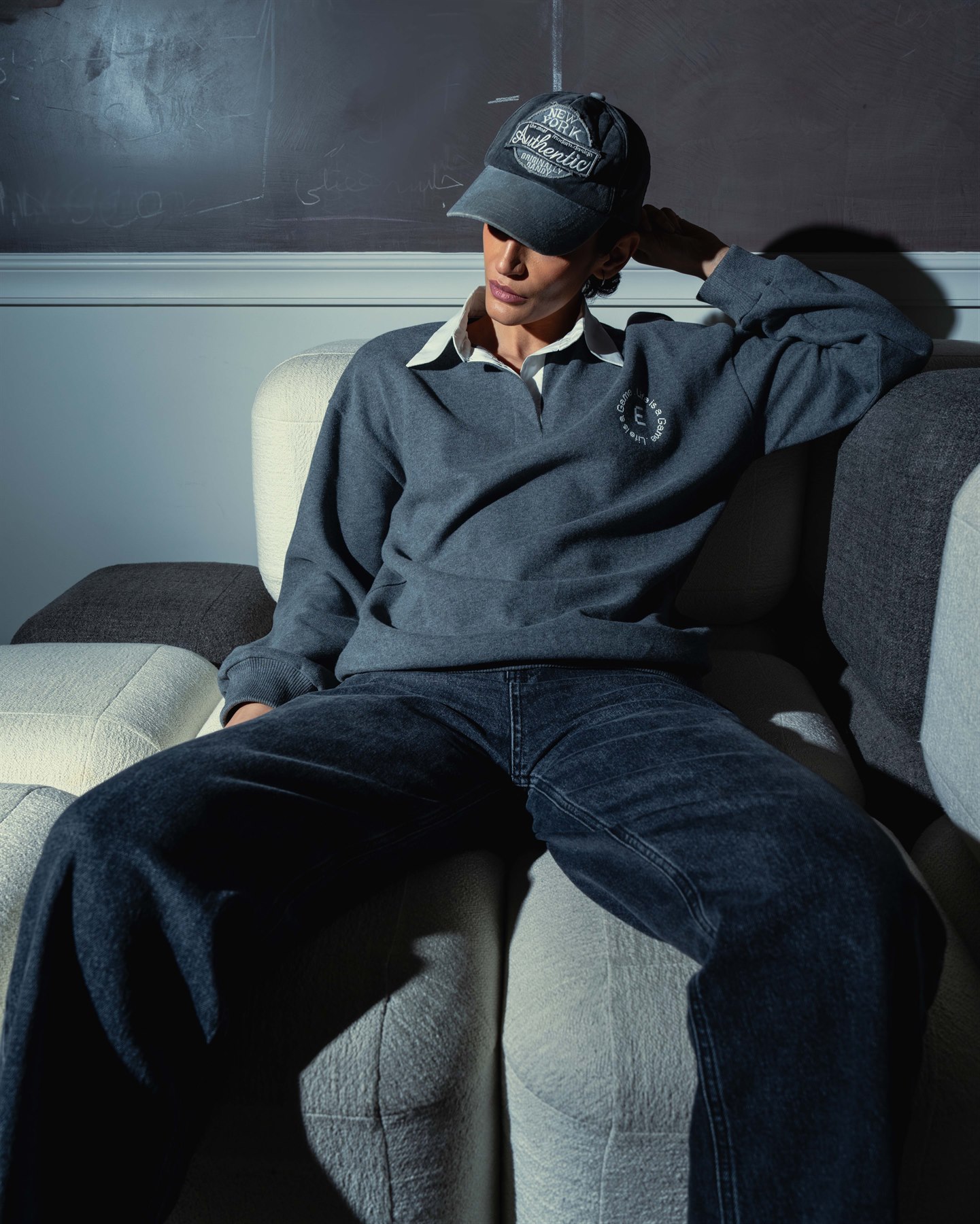 Model wearing a grey relaxed polo, cap and dark denim